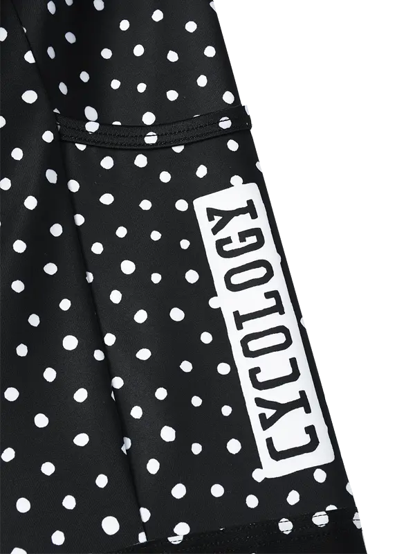 Black and white polka dot cargo cycling shorts with a vertical white brand label reading 'CYOLOGY' on the lower left leg, shown from a side profile view with a pocket against a plain white background.