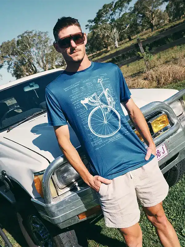 Man wearing blue cycling t-shirt with bike blueprint design, standing by white truck outdoors