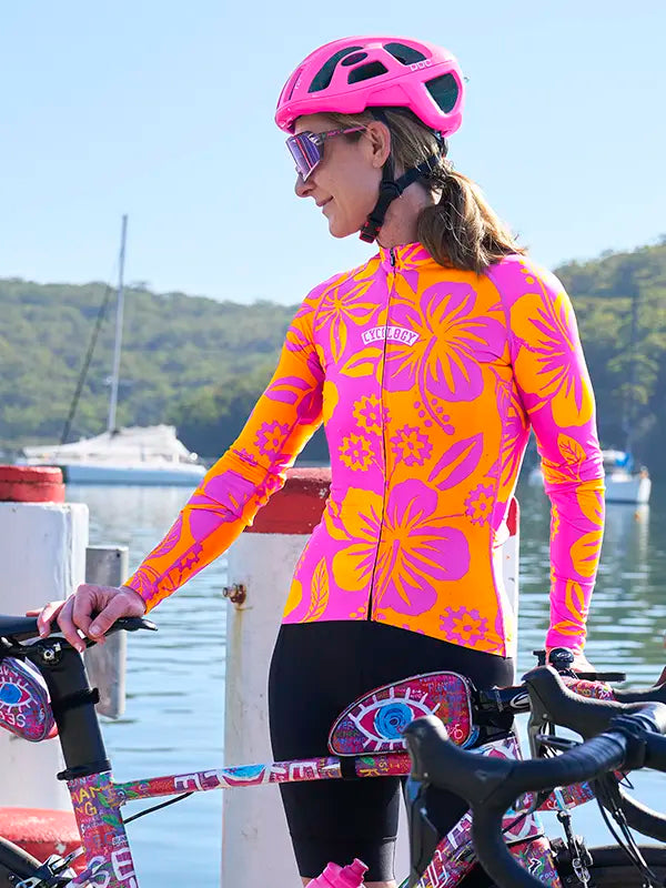 Person wearing a Oahu Pink Women's Long Sleeve Summer Cycling Jersey standing next to a bicycle by a waterfront.