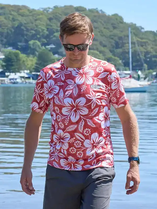 Man wearing red floral cycling t-shirt by water, perfect for summer rides and outdoor adventures
