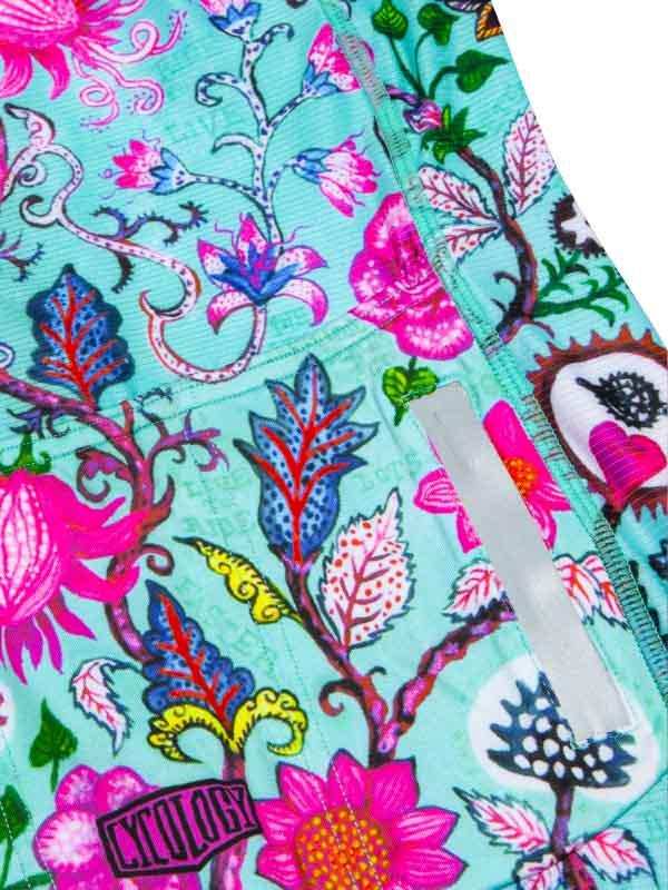 Vibrant floral cycling shorts with pink, blue, and green botanical print, featuring a reflective strip and brand patch.