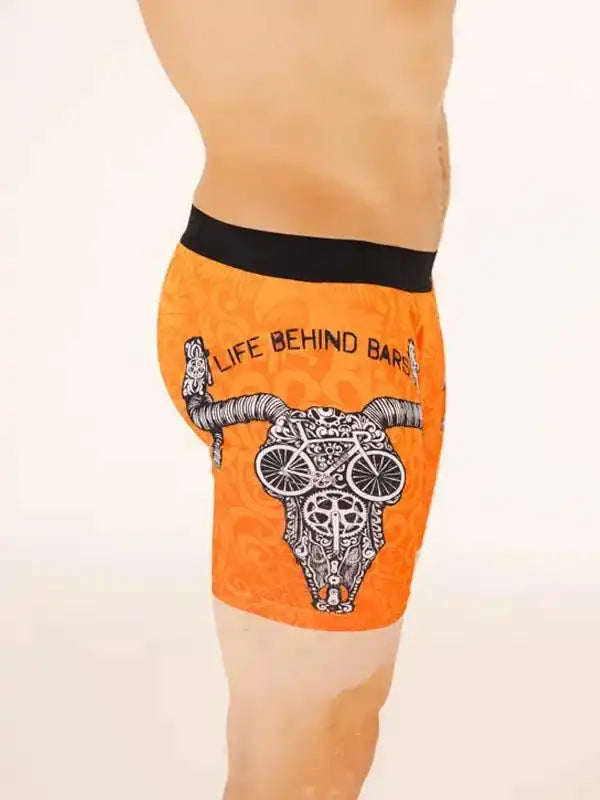 Men's orange cycling shorts with skull and bike wheel design, 'Life Behind Bars' text