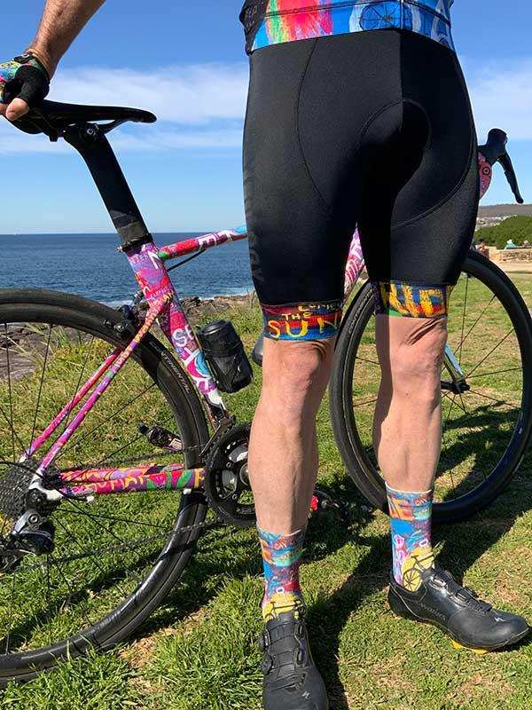 Men's cycling shorts with colorful socks and patterned bike by ocean, ideal for road cycling gear.