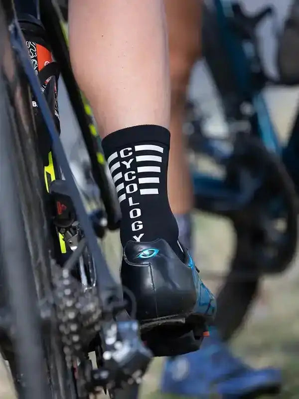Cycling sock with 'CYCOLOGY' text and stripes, worn with clip-in shoe on bike pedal