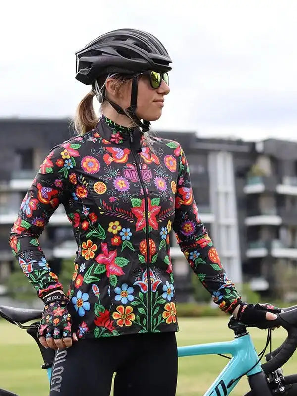 Woman in vibrant floral cycling jersey and helmet, standing with turquoise road bike outdoors