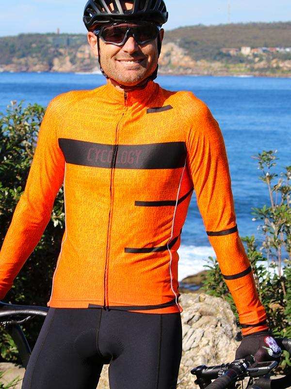 Man in orange cycling jersey with black accents, helmet, and sunglasses, standing by coastal scenery