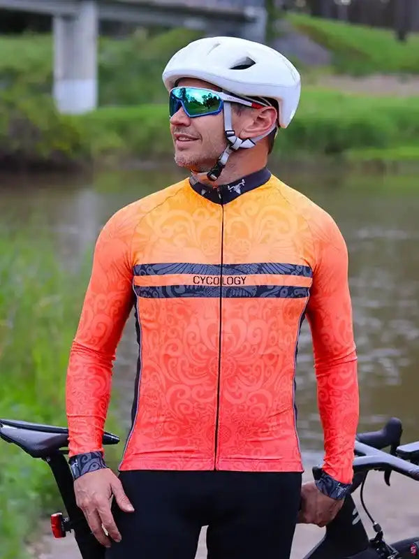 Men's orange cycling jersey with patterned design, worn with helmet and sunglasses near water