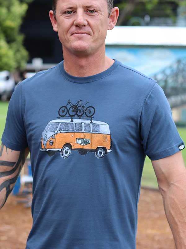 Man wearing blue cycling t-shirt with vintage van and bikes graphic, outdoor setting