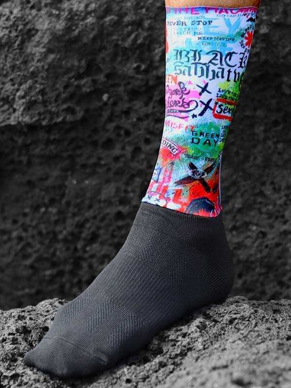 Colorful graphic cycling sock with band names, worn on rocky terrain for outdoor rides