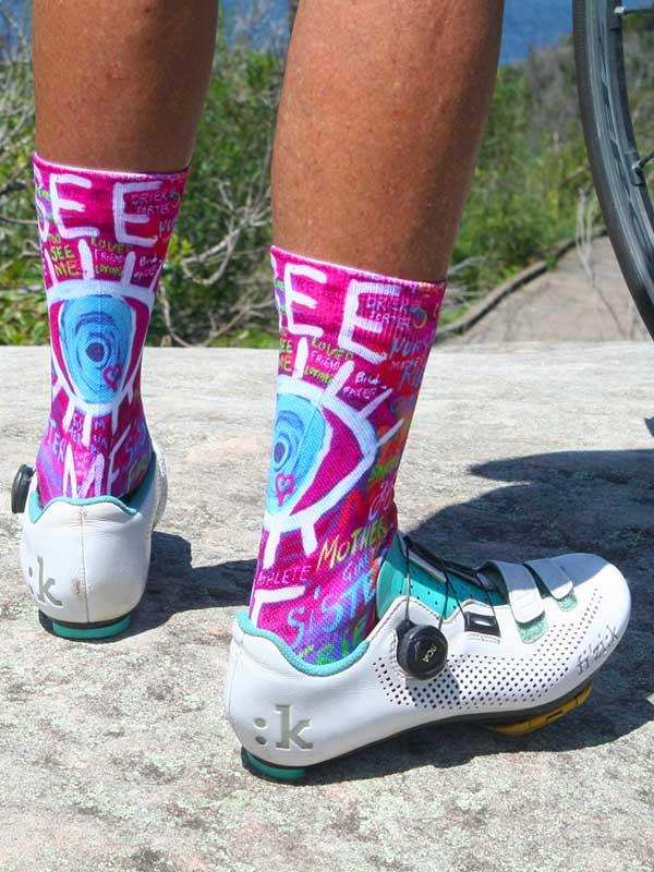 Vibrant pink cycling socks with bold graphic design, worn with white road shoes on outdoor trail