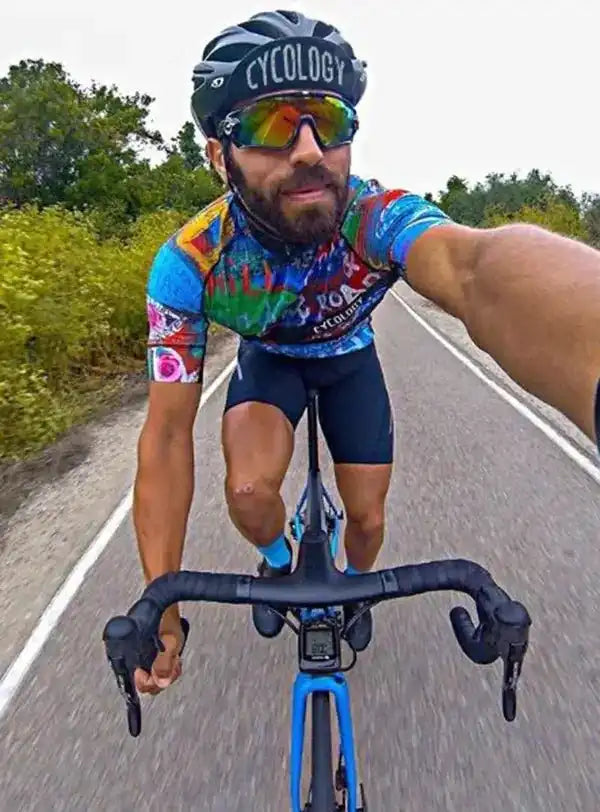 Man cycling in colorful jersey and helmet on road, wearing sunglasses and riding blue bike