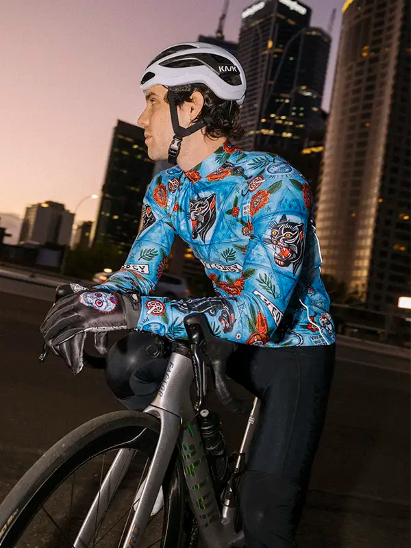 Cyclist wearing a Blue men's Winter  long sleeve cycling jersey with floral and panther design  with a cityscape background