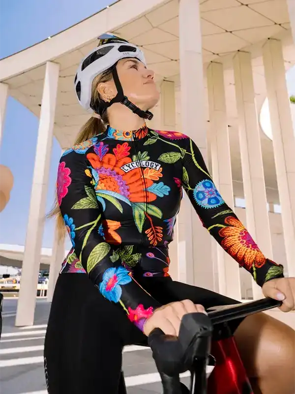 Woman cycling in vibrant floral long-sleeve jersey, black shorts, white helmet, urban setting