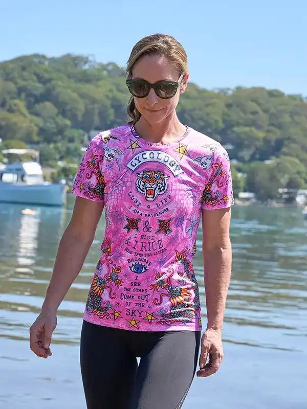 Woman wearing pink graphic cycling jersey with tiger design, walking by water