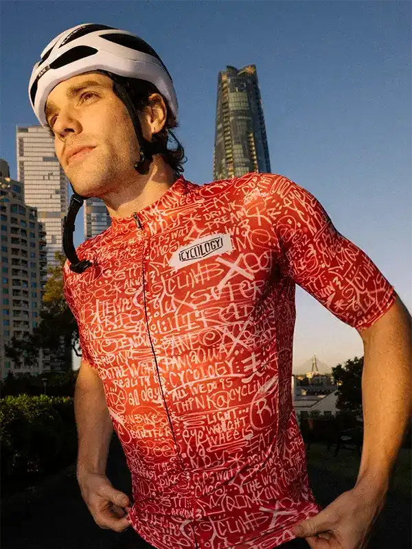 Man wearing red graphic cycling jersey and helmet, urban skyline background, stylish bike apparel