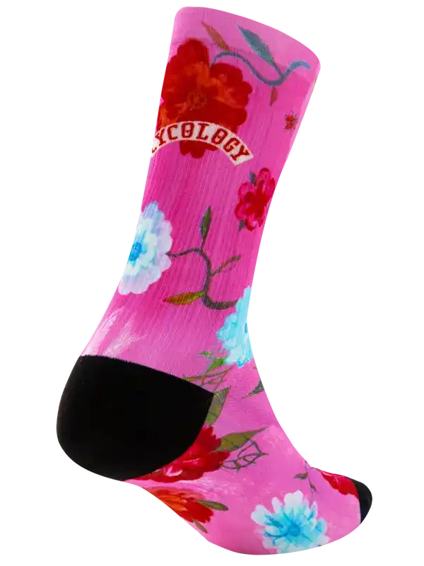 A single crew cycling sock with a bright pink background, featuring a large red flower, a light blue and white flower, and the word 'CYCOLOGY' in a red banner near the upper calf. The sock has a black toe and heel, and is shown on a plain white background.