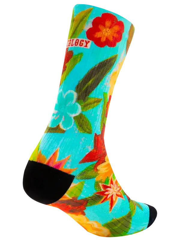 A single crew cycling sock with a bright tropical floral print on a turquoise background, featuring red and white flowers, green leaves, and black heels and toes. The word 'CYCOLOGY' is printed in white on a red tab near the cuff.