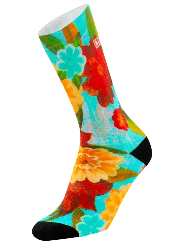 A single crew cycling sock with a vibrant, painterly floral pattern featuring red, orange, yellow, and turquoise flowers on a light blue background, with solid black toes and heels.