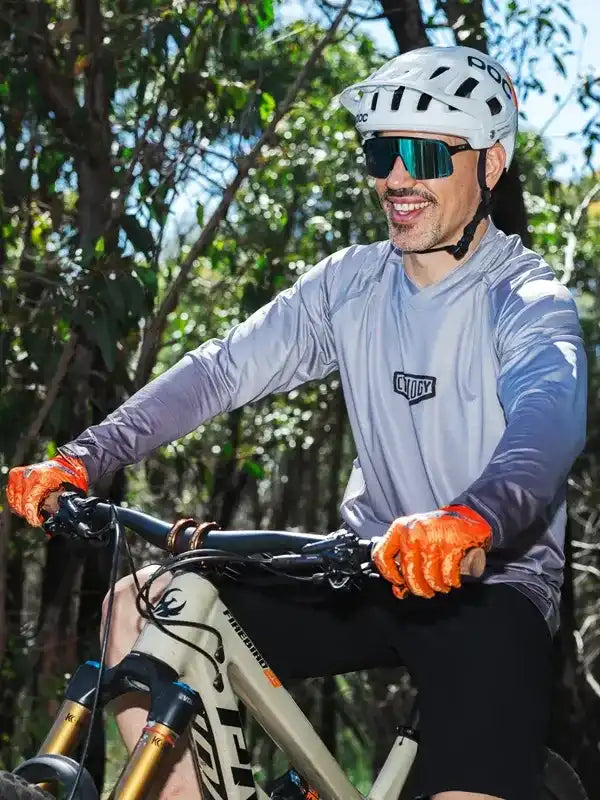 Man riding mountain bike in forest wearing cycling jersey, helmet, and sunglasses