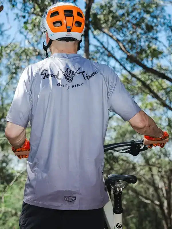 Men's cycling jersey with 'Good Times Quality Dirt' graphic, worn with helmet and gloves on trail ride