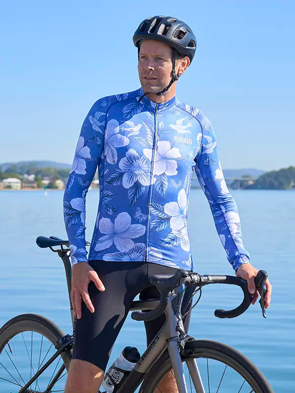 Cyclist wearing a Maui blue floral long sleeve cycling jersey by a lake