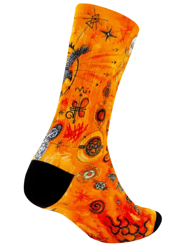 A single crew cycling sock with a vibrant orange and yellow background featuring a detailed art pattern of snakes, stars, and geometric symbols, finished with solid black toes and heels.