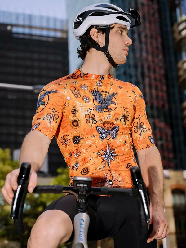 Person wearing an orange cycling jersey with tattoo multi  design, sitting on a bicycle.