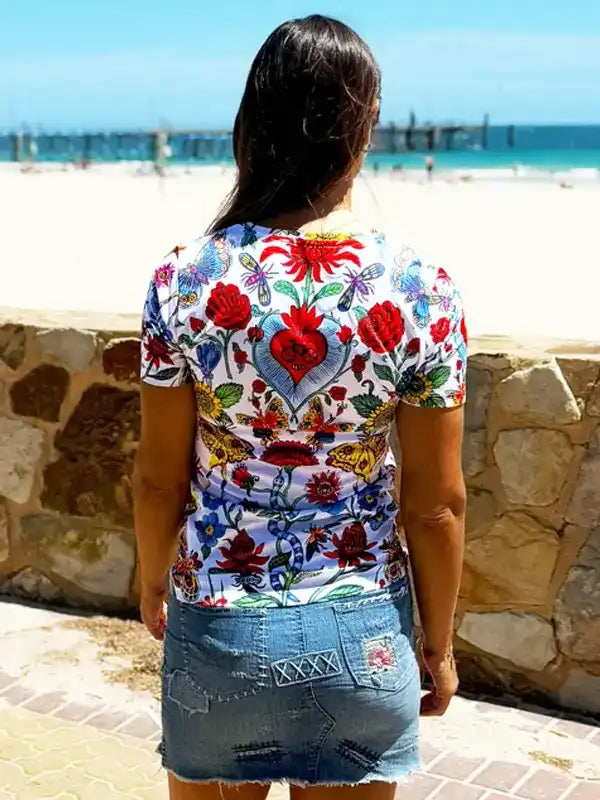 Woman wearing vibrant floral cycling jersey with heart design, beach backdrop, perfect for summer rides.