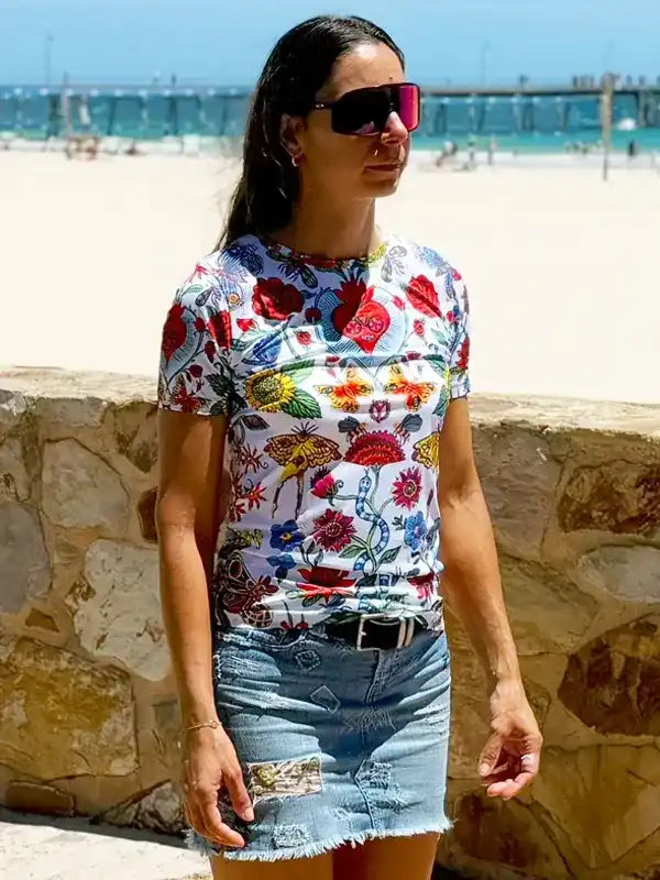 Woman in colorful floral print t-shirt and denim skirt at beach, stylish casual wear