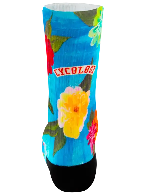 A single crew cycling sock with a bright blue background, featuring a colorful floral print in yellow, pink, red, and green, with a black toe and heel and the word 'CYCOLOG' printed in white on a red banner.