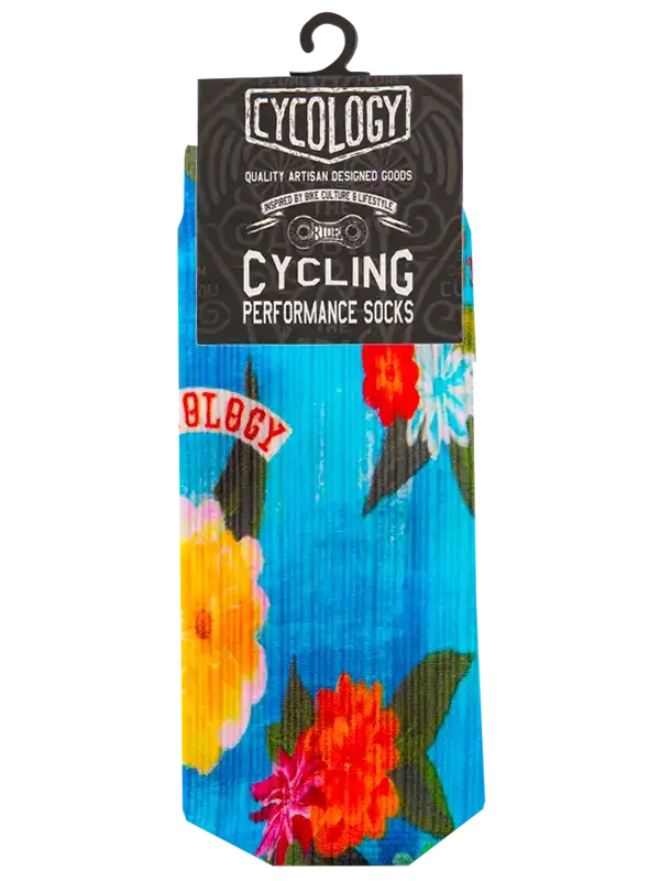 A pair of colorful floral cycling socks in retail packaging with a black header card. The socks feature a bright blue base with large red, yellow, and orange flowers, green leaves, and a red 'CYCOLOGY' patch graphic.