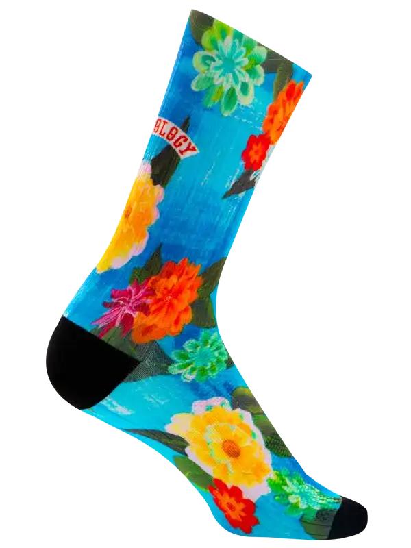 A single crew cycling sock with a bright blue background, featuring a colorful floral print in yellow, pink, red, and green, with a black toe and heel and the word 'CYCOLOGY' printed in red on a white banner.
