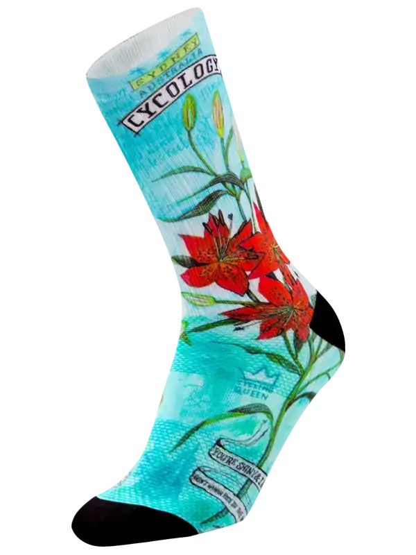 A single crew cycling sock with a light blue and white watercolor background, featuring red lily flowers, green stems, and black toe/heel accents. The sock has text graphics including 'CYCOLOGY' and 'The Science of Socks'.