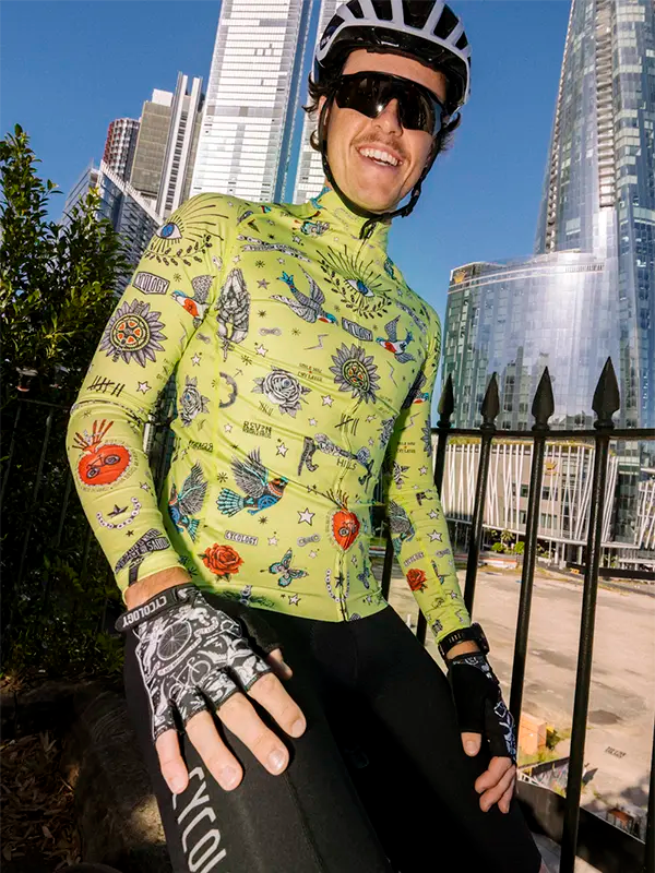 Person wearing a colorful lime green long sleeve cycling jersey with tattoos in an urban setting