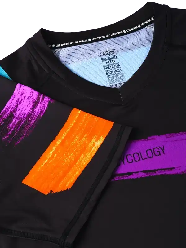 Black cycling jersey with vibrant purple and orange brushstroke design, performance fabric label visible
