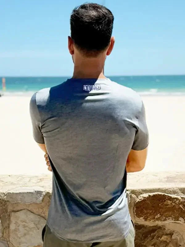 Man wearing grey cycling t-shirt with blue gradient back, standing by beach, ideal for active wear