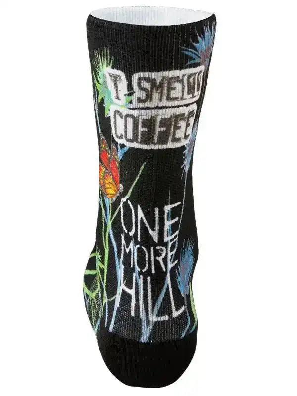 Black cycling sock with 'I Smell Coffee One More Hill' graphic, butterfly, and plant design for cyclists
