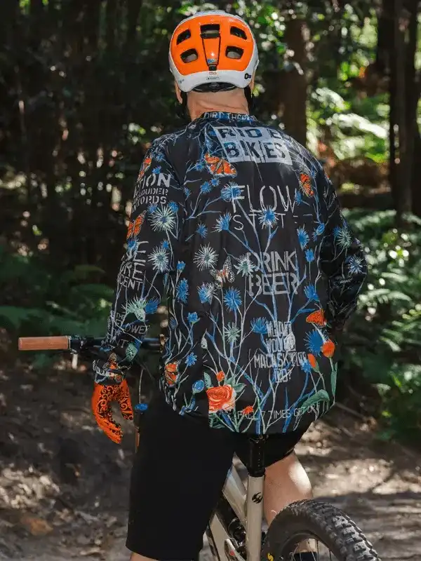 Men's cycling jersey with floral print and bold text, worn on forest trail ride