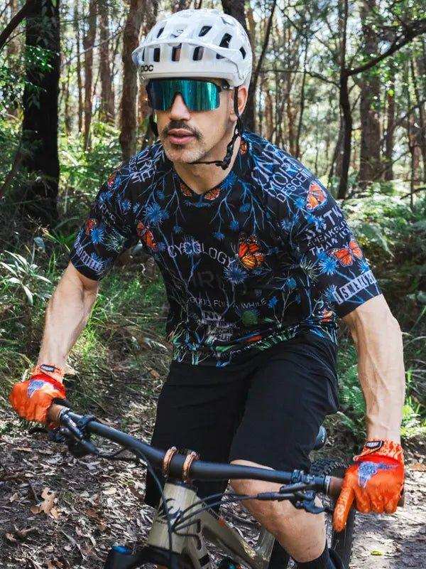 Man mountain biking in forest wearing floral cycling jersey, helmet, and sunglasses