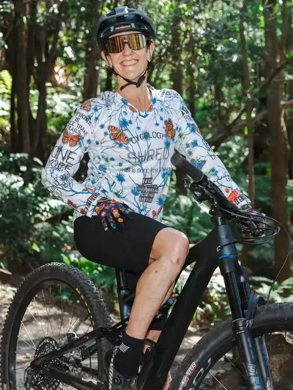 Woman in floral cycling jersey and shorts riding mountain bike in forest trail