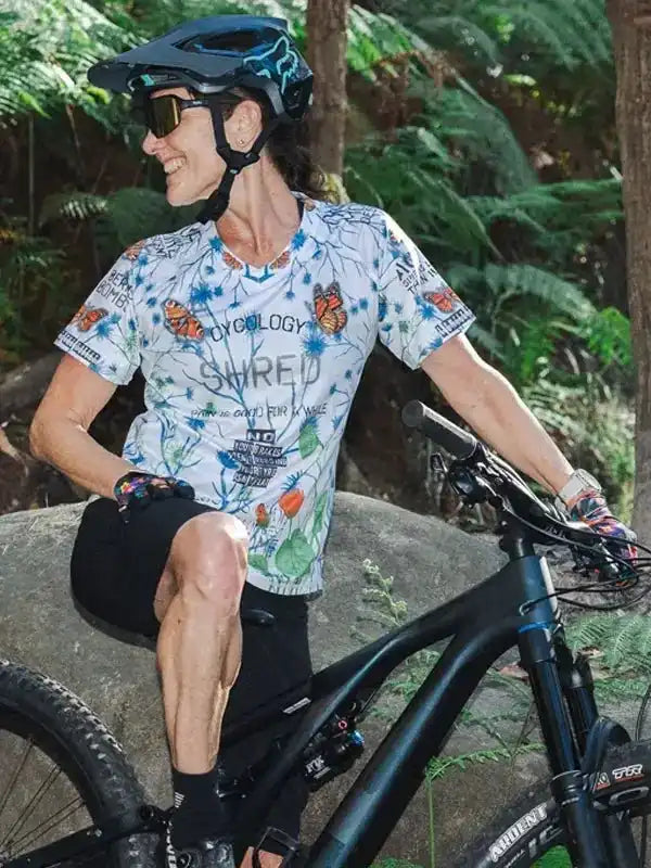 Woman in butterfly print cycling jersey and helmet, riding mountain bike in forest trail