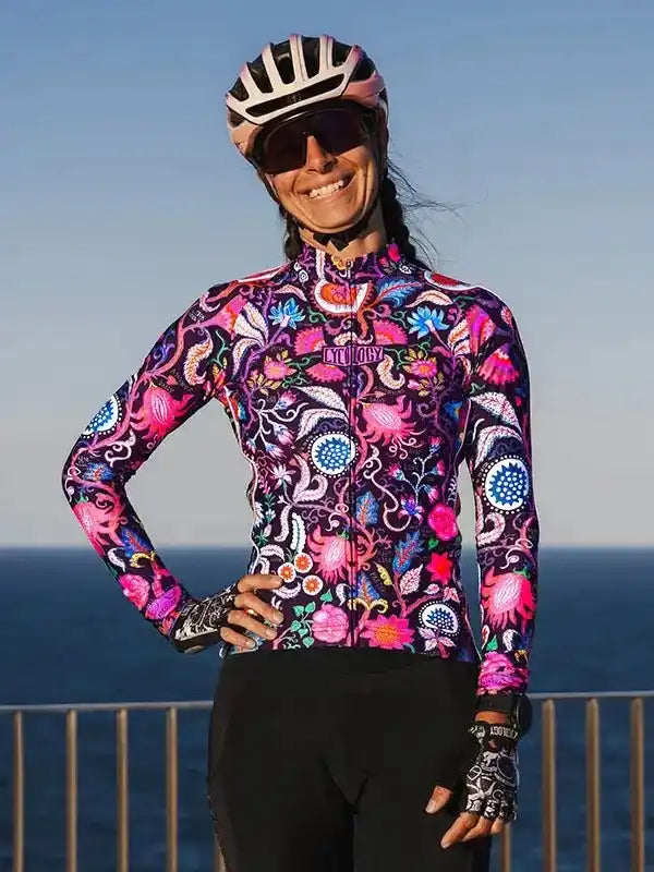 Woman in vibrant floral cycling jersey and helmet, ocean backdrop, stylish bike wear for road rides