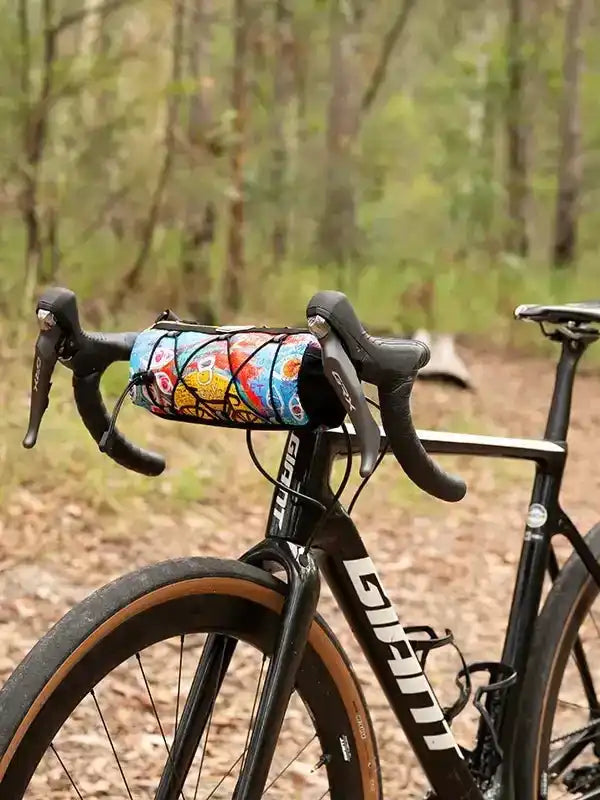 Colorful cycling handlebar bag on road bike in forest trail, perfect for bike rides and outdoor adventures.