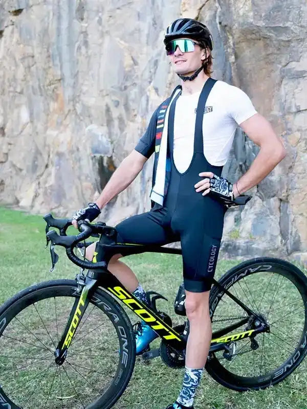 Cyclist in black bib shorts and white jersey with Scott bike, rocky outdoor setting