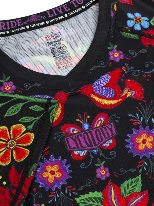 Black cycling jersey with vibrant floral and bird print, featuring 'Live to Ride' collar text and performance fabric tag