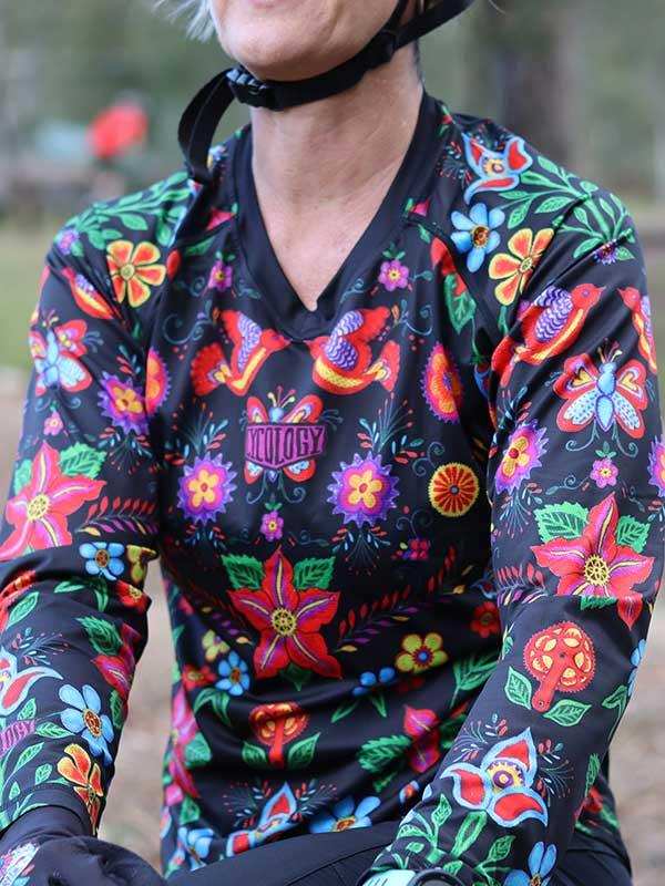 Woman wearing vibrant floral cycling jersey with long sleeves, ideal for road or mountain biking adventures.