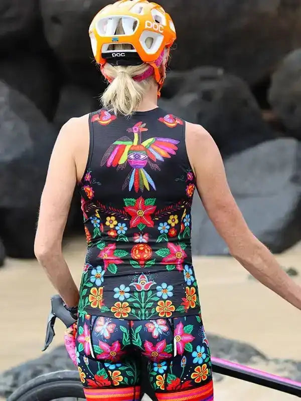 Woman in colorful floral cycling jersey and shorts, wearing POC helmet, back view near rocks