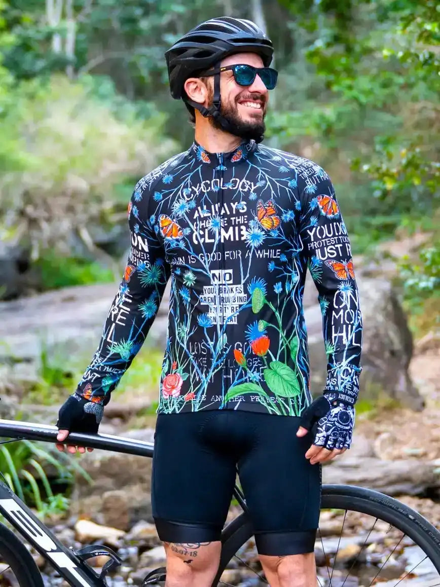 Man in floral cycling jersey and black shorts, smiling beside bike on forest trail