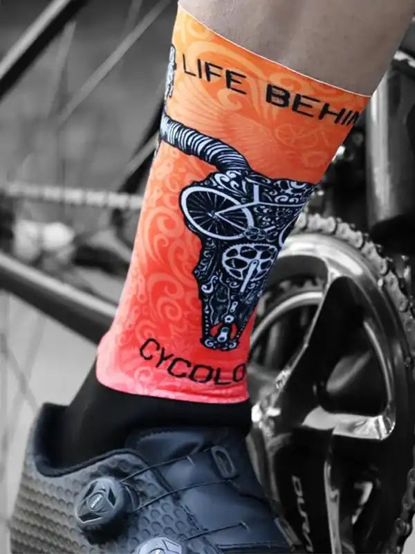 Orange cycling sock with skull and bike design, worn with cycling shoe near bike gear