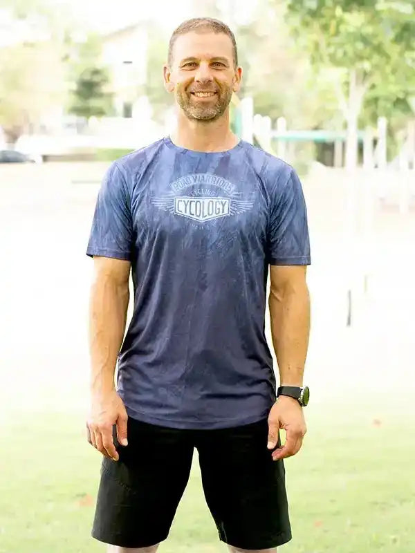 Man wearing blue cycling t-shirt with 'Cycology' graphic, black shorts, outdoors on grass